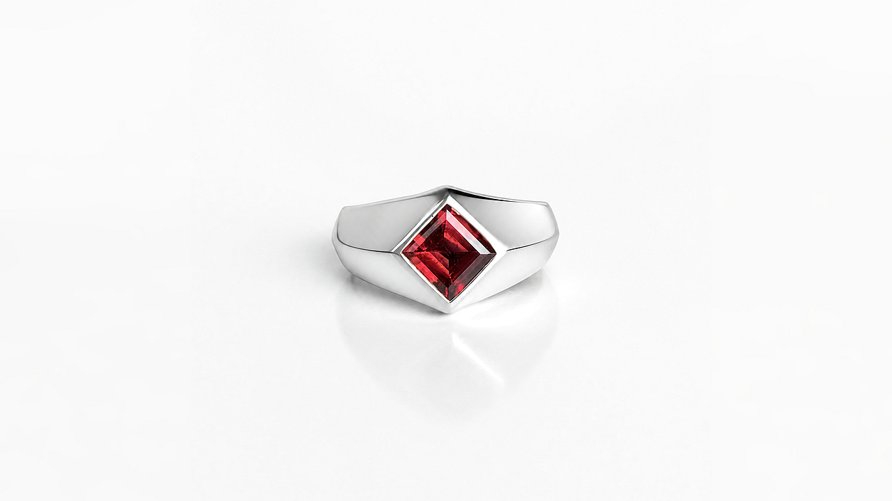 Silver signet ring seen from the front at an angle, a red garnet set as a rhombus at its centre.